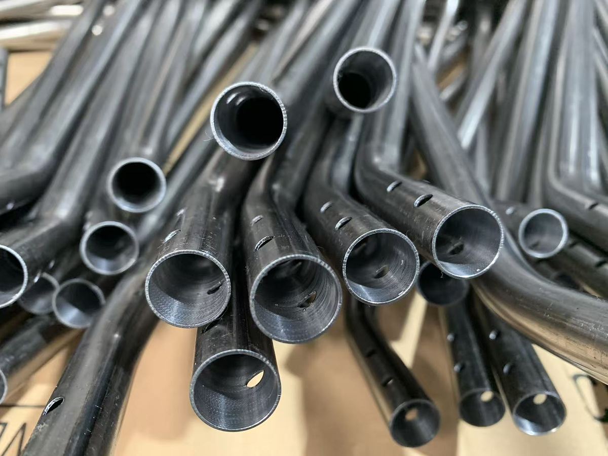 Cut and drilled ends of coated bent steel tube in a production batch